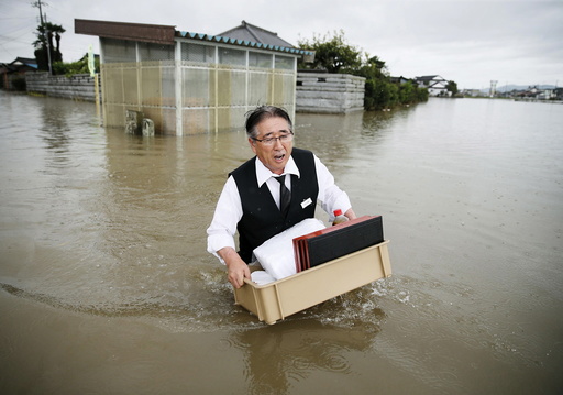 A man holding a tray of belongings wades through a road at an area flooded by the Omoigawa river, caused by typhoon Etau in Oyama