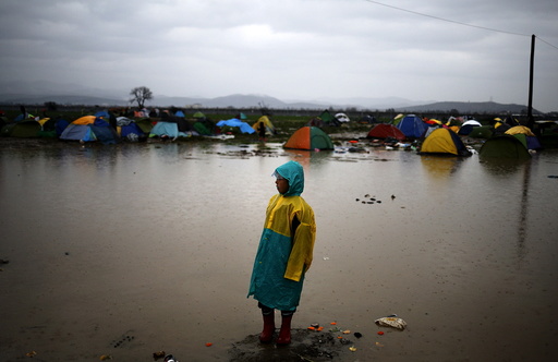 A migrant boy stands near a flooded muddy field as it rains at a makeshift camp on the Greek-Macedonian border, near the village of Idomeni