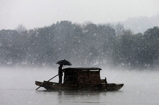 A man holds an umbrella to shield against snowfall as he rows a boat on the West Lake in Hangzhou