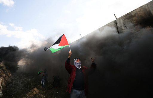 Protester holds a Palestinian flag during clashes with Israeli troops at a protest marking the 12th anniversary of a campaign against the Israeli barrier, in the West Bank village of Bilin near Ramallah