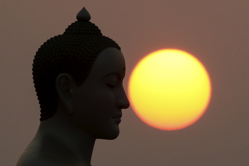 The sun rises next to a Buddha statue while monks and novices gather to receive alms at Wat Phra Dhammakaya temple, in what organizers said was a meeting of over 100,000 monks in Pathum Thani