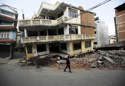 A man walks past a damaged and collapsed five-storey house, a month after the April 25 earthquake in Kathmandu