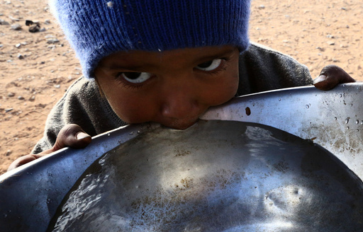 Stateless Arab boy from an ethnic group known as Bedoon, who are believed to be descendants of nomadic Bedouins, drinks water from a pot in a desert west of Al-Jawf region