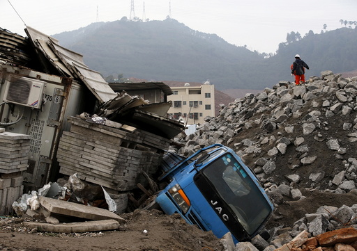 Rescue workers walk past a damaged vehicle in the industrial park hit by a landslide in Shenzhen