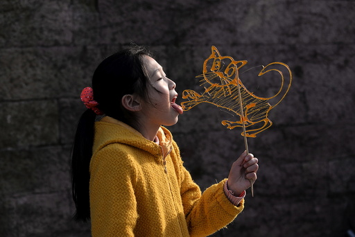 A girl licks a traditional candy in the shape of a tiger at a folk art exhibition in Ningbo