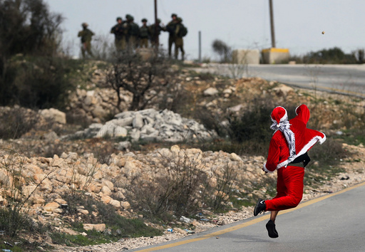 Palestinian demonstrator dressed as Santa Claus hurls stones towards Israeli troops during clashes at a protest near the West Bank city of Ramallah