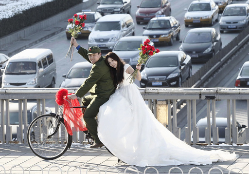 An engaged couple sit on a bicycle as they pose for wedding photographs to the theme of 