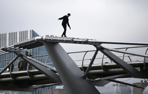 A man balances as he walks on the support structure of the Millennium Bridge in London
