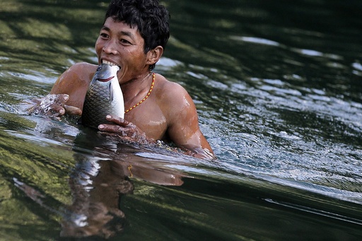 A Naga man carries fish in his teeth after it was stunned by dynamite in a creek between Donhe and Lahe township in the Naga Self-Administered Zone