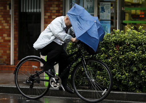 A man holding onto an umbrella as he cycles in heavy rain caused by typhoon Etau in Tokyo's business district