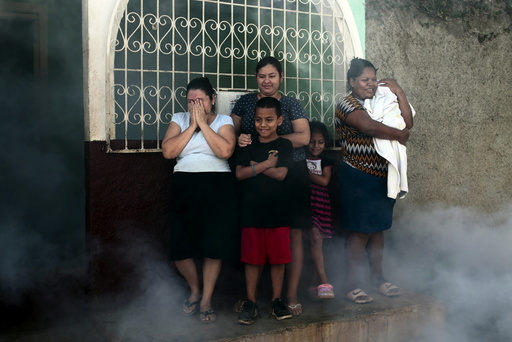 People stand outside their house while a health ministry worker fumigates to kill mosquitoes during a campaign against dengue and chikungunya in Managua