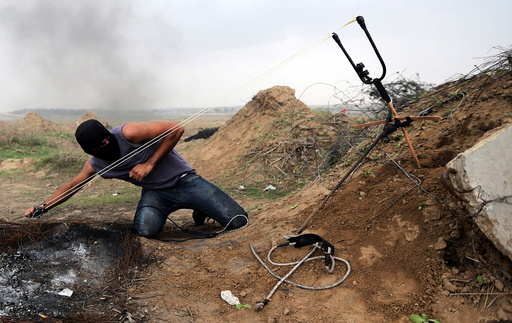 Palestinian protester uses sling shot to hurl stones at Israeli troops during clashes near border between Israel and Central Gaza Strip