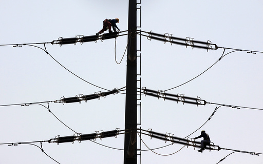 Employees of K-Electric fix cables on a power transmission tower in Karachi,