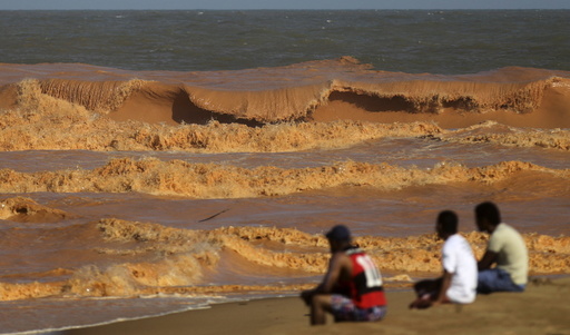 Men look on from the banks of Rio Doce (Doce River), which was flooded with mud after a dam owned by Vale SA and BHP Billiton Ltd burst, as the river joins the sea on the coast of Espirito Santo in Regencia Village, Brazil