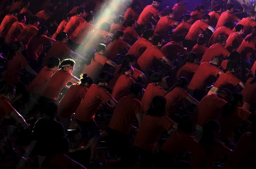 A participant is seen under a beam of light as hundreds of people ride indoor bicycles during a campaign to promote body-building exercises at a gymnasium in Kunming