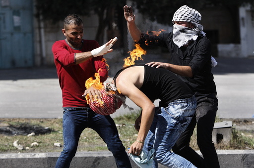 Palestinian protesters put out a fire burning on a compatriot, caused by a molotov cocktail which he was trying to hurl at Israeli troops during clashes in the West Bank city of Hebron