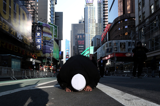 A Muslim man kneels on Broadway Ave. as he takes part in afternoon prayers during an 