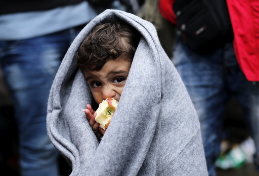 A migrant child eats an apple as he waits next to the border crossing with Croatia near the village of Berkasovo