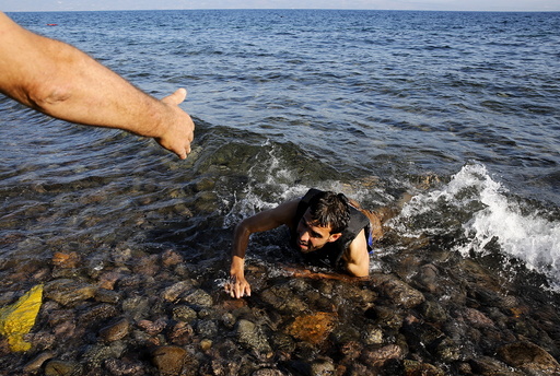 A local man helps a Syrian refugee who jumped off board from a dinghy as he swims exhausted at a beach on the Greek island of Lesbos