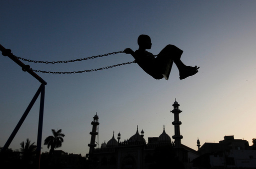 A boy is silhouetted as he plays on a swing during sunset hours near a mosque in Karachi,
