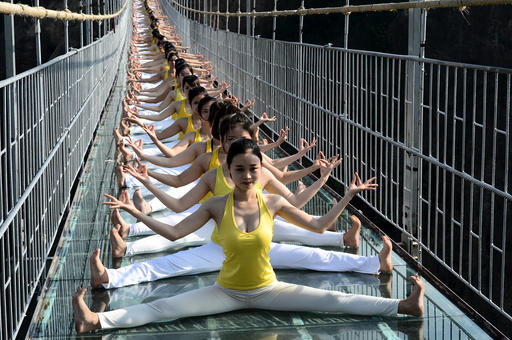 Women practice yoga during a performance on a glass bridge at the Shiniuzhai National Geo-park in Pingjiang county