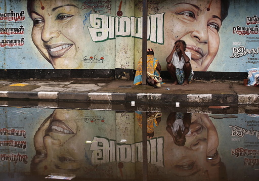 A flood-affected couple sits along a flooded roadside under a picture of Jayalalithaa, CM of Tamil Nadu, in Chennai