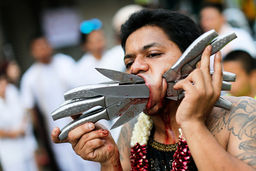 A devotee of the Chinese Ban Tha Rue shrine with knives piercing his face takes part in a procession celebrating the annual vegetarian festival in Phuket