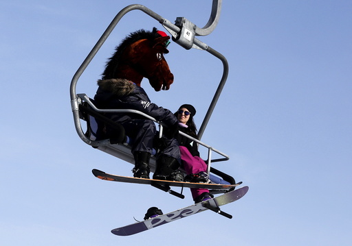 A snowboarder wearing a mask of a horse head rides a lift uphill at the Bobrovy Log ski resort in the suburbs of Krasnoyarsk