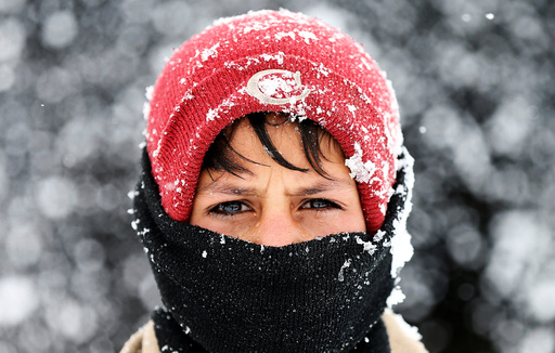 An Internally displaced Afghan boy looks on as he stands outside his shelter during a snowfall in Kabul