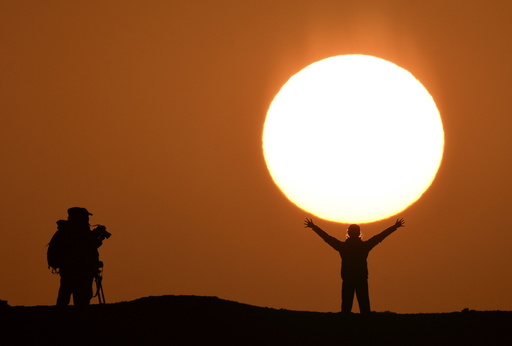 A tourist poses for photographs in front of the rising sun at a tourist resort in Bayingolin Mongol Autonomous Prefecture