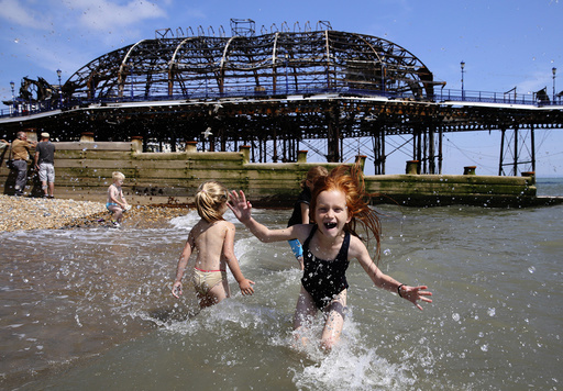 Seven year old Lily Blackburn plays with friends in the sea near the burnt remains of a section of Eastbourne pier, in Eastbourne
