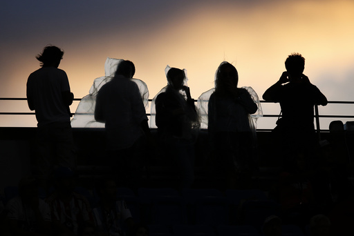 Fans wearing rain ponchos are backlit as they watch the sunset from Arthur Ashe Stadium ahead of the mens final between Federer of Switzerland and Djokovic of Serbia at the U.S. Open Championships tennis tournament in New York