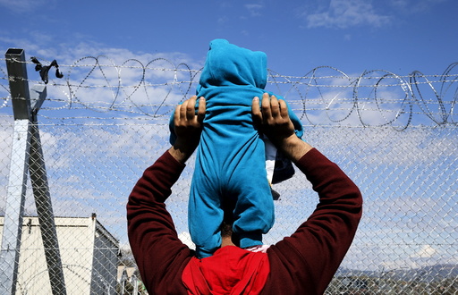 A stranded refugee lifts his child in front of a fence as he and hundreds of others take part in a protest at the Greek-Macedonian border near the Greek village of Idomeni