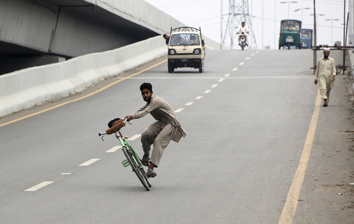 Man does tricks on his bicycle on a highway as the Eid holiday begins in Peshawar
