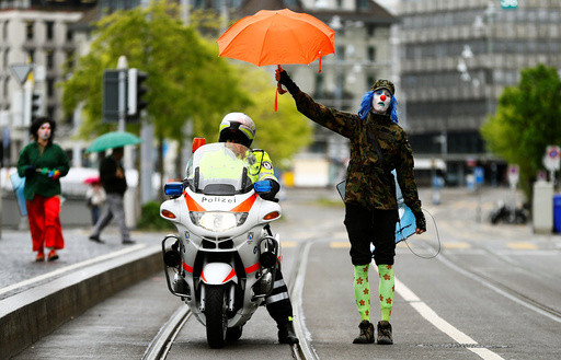 A protester dressed as a clown holds an umbrella over a Swiss police officer on a motorbike during a May Day demonstration in Zurich