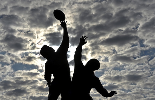The sun rises behind a statue of rugby players reaching for the ball, outside Twickenham rugby stadium in west London