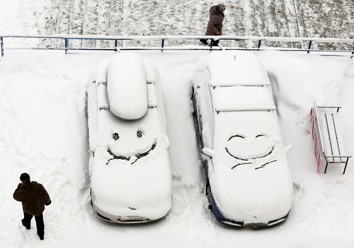 People walk past cars with faces which are scrawled on windscreens covered with snow after snowfall in Krasnoyarsk
