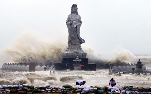 People set up sand bags to reinforce an embankment in front of an Avalokitesvara Bodhisattva statue as waves brought by Typhoon Dujuan slam the coastline in Quanzhou