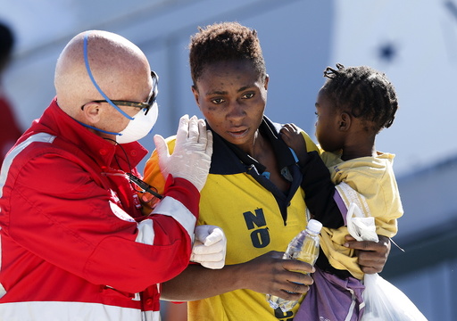 A rescue worker helps a woman with her son as they disembark the Italian naval vessel Cigala, in the Sicilian harbour of Augusta