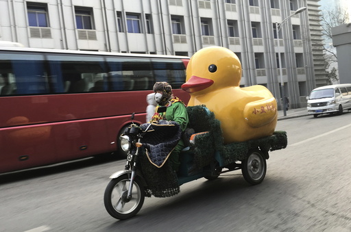 A man wearing a mask and dressed in a clown costume rides an electric tricycle while carrying a container in the shape of a rubber duck amid heavy smog in Beijing
