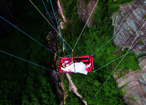 A newly married couple lie on a canvas mat as they are lowered from a glass bridge during a promotional event for the tourist spot, on Chinese Valentines' Day in Pingjiang