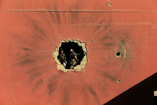 Policemen look through a hole in a house from the clashes in Qaraqosh